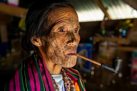 Chin woman with spiderweb tattoo smoking a pipe