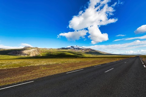 Asphalt road through barren volcanic landscape with view of snow-capped volcano Snaefellsjoekull