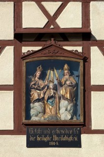 Figures of the Trinity in a glass shrine in the facade of a farmhouse
