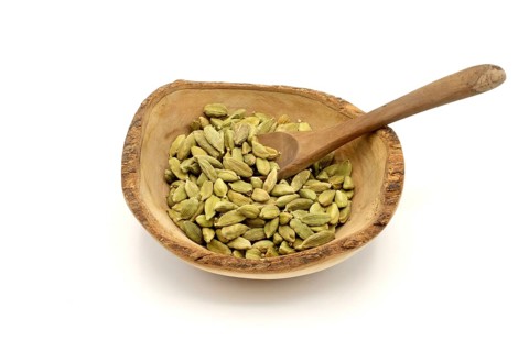Cardamom pods in a wooden rustic bowl with a wooden spoon against a white background