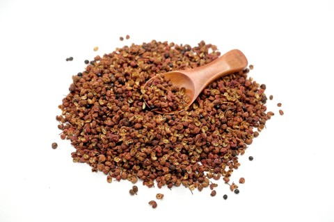 Sichuan peppercorns with a wooden spoon against a white background