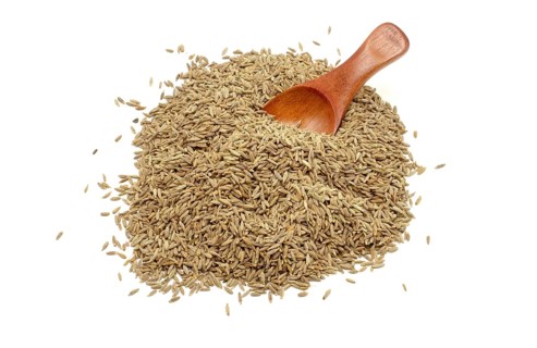 A pile of cumin seeds with a wooden spoon against a white background