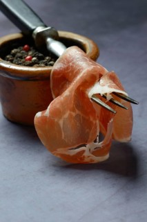 A slice of coppa on fork and clay pot with peppercorns
