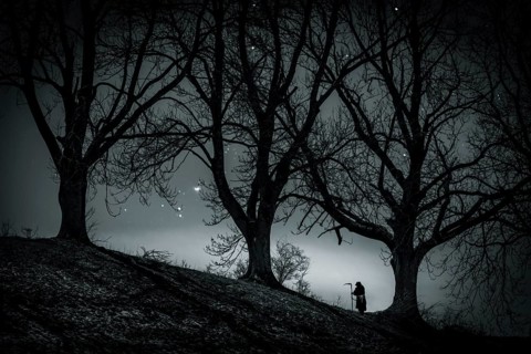 Man with scythe under tree with starry sky