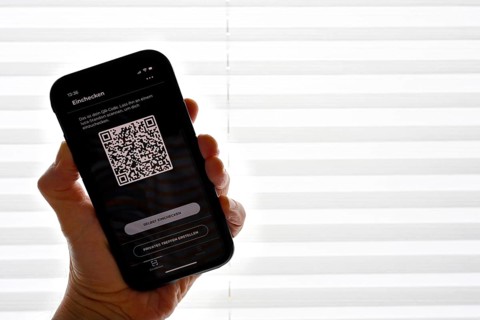 Hand holds smartphone with Luca app with QR code in front of window
