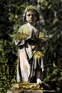 Praying grave sculpture with moss at Melaten cemetery