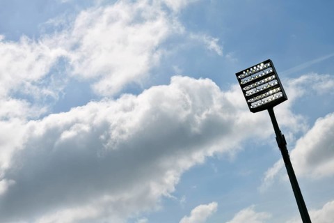 Floodlight mast switched on in front of blue sky with clouds