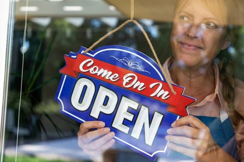 Happy Female Store Owner Turning Open Sign in Window