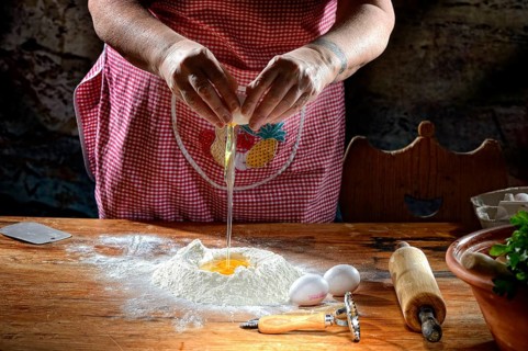 Woman beats egg on flour for pasta dough