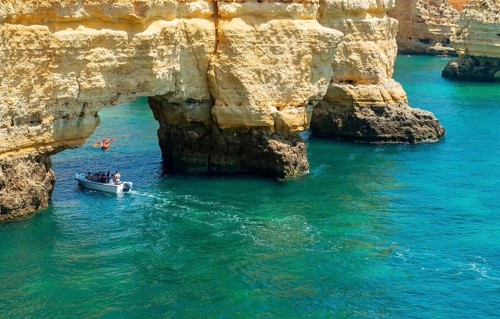 Excursion boat sails through rock arch in turquoise sea