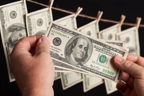 Male hands holding hundred dollar bills with several hanging from a clothesline on a dark background