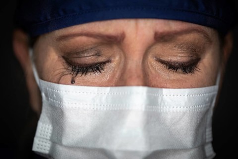 Tearful stressed female doctor or nurse wearing medical face mask on dark background