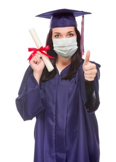 Graduating female wearing medical face mask and cap and gown give a thumbs up isolated on a white background