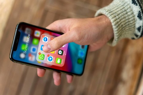 Hand haelt iPhone 11 Pro mit App-Icons von Messenger Diensten und Sozialen Netzwerken