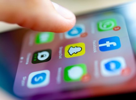 Finger tapping on screen with app icons of messenger services and social networks