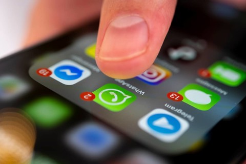 Finger tapping on screen with app icons of messenger services and social networks