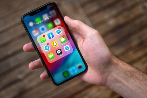 Hand haelt iPhone 11 Pro mit App-Icons von Messenger Diensten und Sozialen Netzwerken