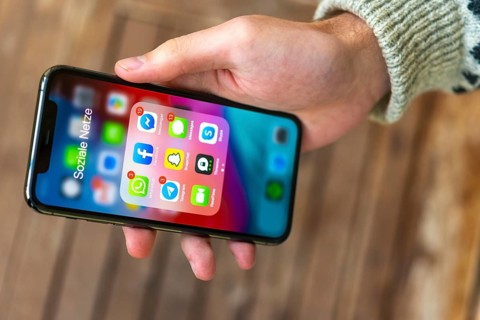 Hand haelt iPhone 11 Pro mit App-Icons von Messenger Diensten und Sozialen Netzwerken
