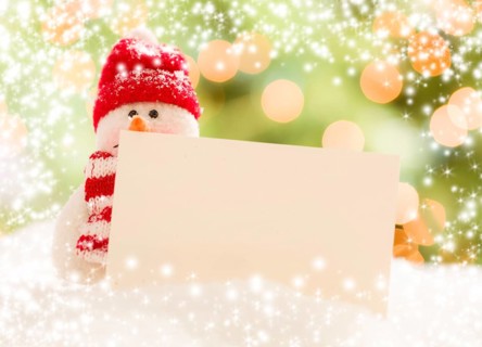Cute snowman with scarf and hat next to blank white card over abstract snow and light background