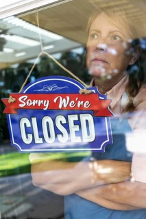 Sad female store owner turning sign to closed in window