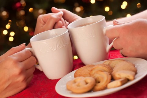 Man and woman sharing hot chocolate and cookies in front of holiday lights