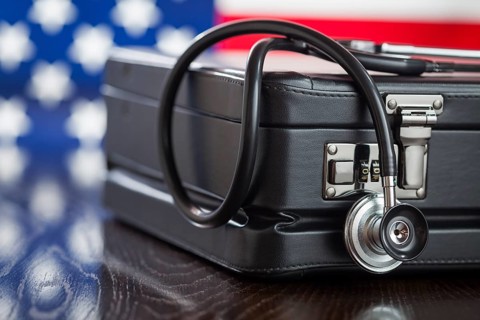 Leather briefcase and stethoscope resting on table with american flag behind