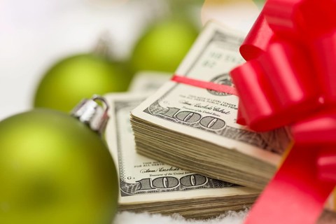 Stack of one hundred dollar bills with red bow near green christmas ornaments on snow flakes