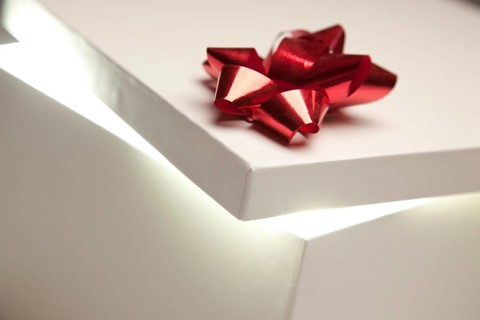 Gift box with red bow lid revealing very bright contents on a gradated background