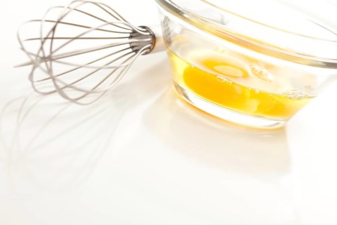 Hand mixer with eggs in a glass bowl on a reflective white background