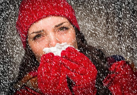 Sick mixed-race woman wearing winter hat and gloves blowing her sore nose with a tissue in the snow