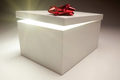 Gift box with red bow lid revealing very bright contents on a gradated background