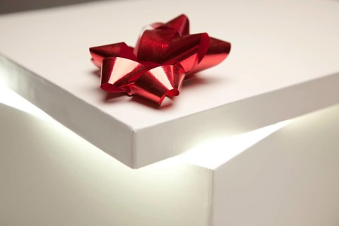 Gift box with red bow lid revealing very bright contents on a gradated background