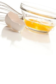 Hand mixer with eggs in a glass bowl on a reflective white background
