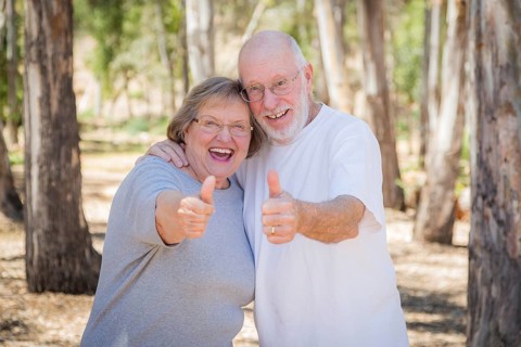 Happy senior couple with thumbs up outdoors