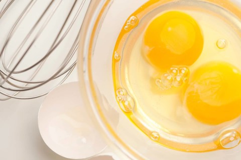 Hand mixer with eggs in a glass bowl on a reflective white background