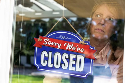 Sad female store owner turning sign to closed in window