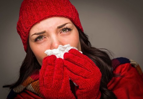 Sick mixed-race woman wearing winter hat and gloves blowing her sore nose with a tissue