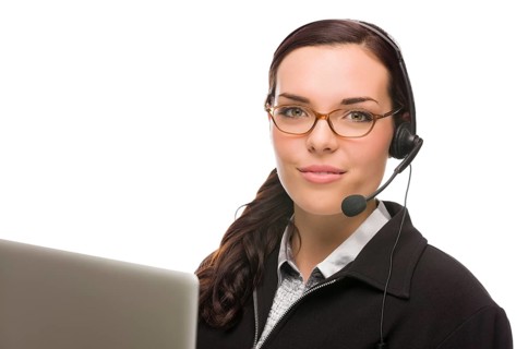 Helpful mixed-race receptionist in front of computer wearing phone head-set isolated on white background