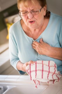 Grimacing senior adult woman at kitchen sink with chest pains