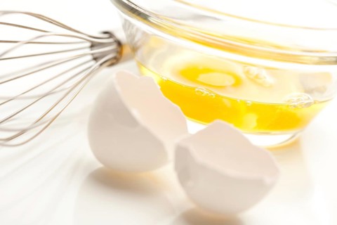 Hand mixer with eggs in a glass bowl on a reflective white background