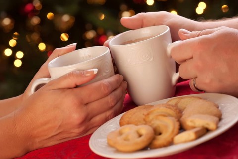Man and woman sharing hot chocolate and cookies in front of holiday lights