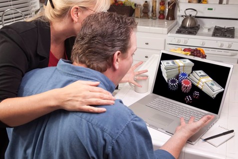 Couple in kitchen using laptop with stacks of money and poker chips on the screen