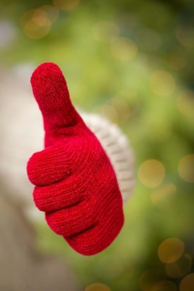 Woman in sweater with seasonal red mittens holding out a thumb up sign with her hand