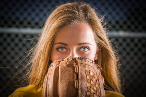 Dramatic young woman with softball glove covering her face outdoors