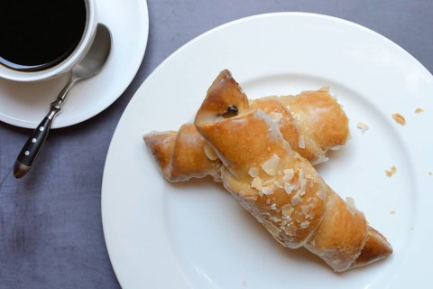 Almond croissant on plate with coffee cup