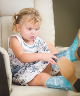 Adorable blonde haired blue eyed little girl putting on cowboy boots