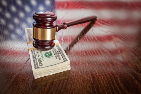 Wooden gavel resting on stack of money with american flag reflection on table