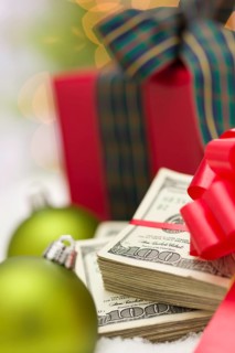 Stack of one hundred dollar bills with red bow near green christmas ornaments and wrapped gift box on snow flakes