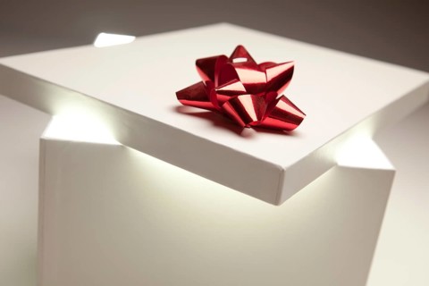 Gift box with red bow lid revealing very bright contents on a gradated background