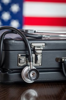 Leather briefcase and stethoscope resting on table with american flag behind